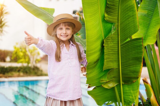 Little girl in a beautiful pool with palms in the background she is showing a thumbs up sign