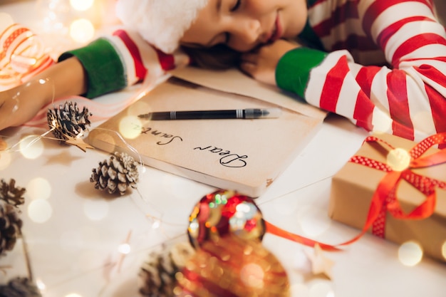 A little girl before Christmas writes a letter to Santa Claus on the table with garlands. child writes a letter to santa claus.