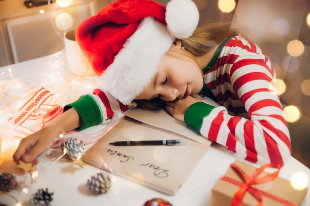 A little girl before Christmas writes a letter to Santa Claus on the table with garlands. child writes a letter to santa claus.