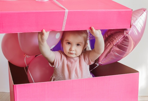 Little girl in a big pink gift box with balloons