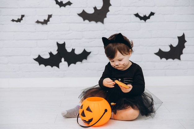 A little girl in a black cat costume with pumpkin basket holding a gingerbread