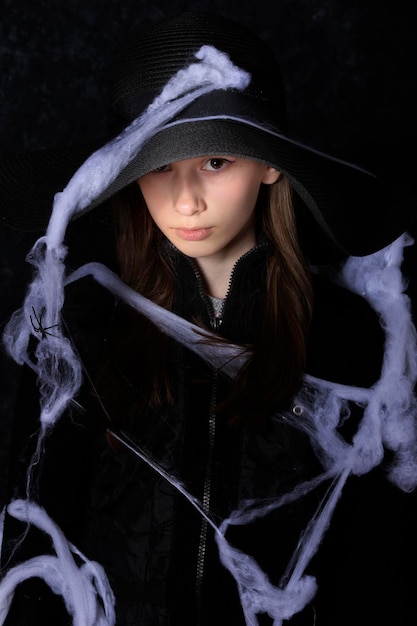 Photo little girl in a black hat on a halloween spider web