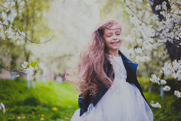 Little girl in black jacket and white dress running in the spring cherry garden