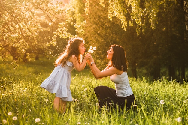 Little girl blowing dandelion in park with her mother