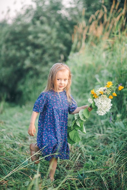 A little girl in a blue dress holds a bouquet of flowers.