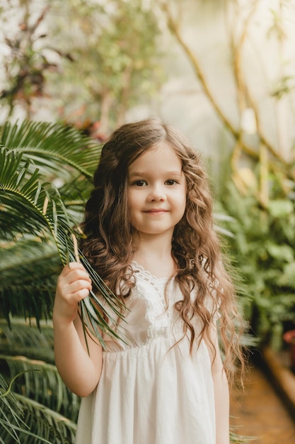 Little girl in the botanical garden a girl in a white dress laughs near palm leaves