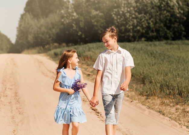 Little girl and boy brother and sister holding hands in nature on a sunny day. Kids in the country.