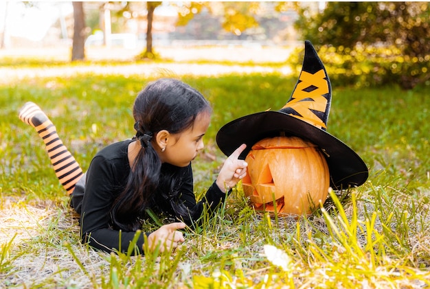 Little girl and boy carving pumpkin at Halloween. Dressed up children trick or treating. Kids trick or treat. Child in witch costume playing in autumn park. Toddler kid with jack-o-lantern.