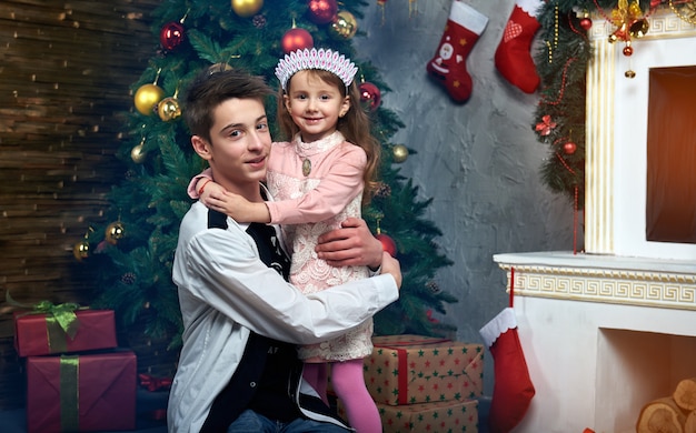 A little girl and a boy near the tree by the fireplace with gifts.