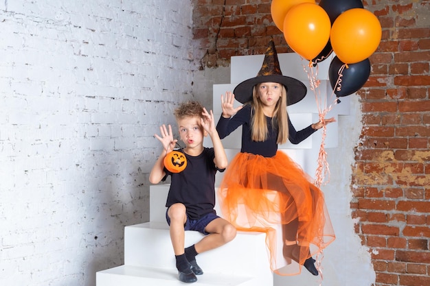 A little girl and a boy in witch and sorcerer costumes with hats holding orange and black balls and making frightening gestures