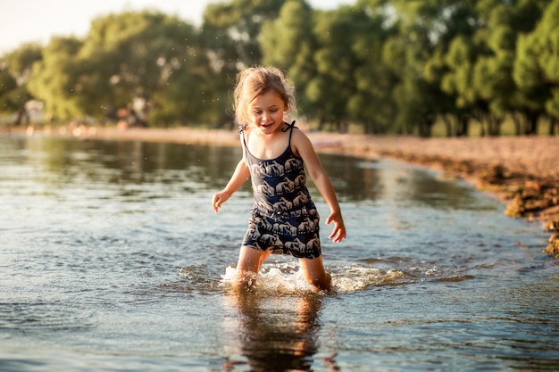 little girl by the river in summer splashes water