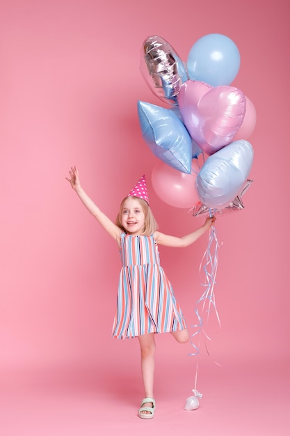 Little girl in a cap on her head with balloons on a pink surface