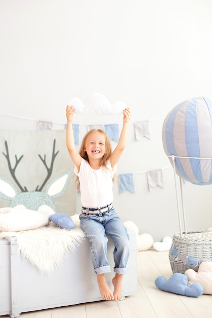 A little girl in casual clothes holds a cloud pillow of a decorative balloon. The child plays in the children's room. The concept of childhood. birthday, holiday decorations