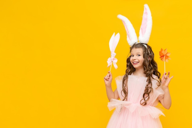 A little girl celebrates Easter A happy smiling child is holding some origami flowers A charming teenager with rabbit ears on a yellow isolated background Copy space Banner