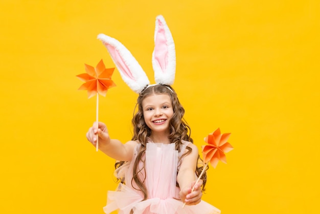 A little girl celebrates Easter A happy smiling child is holding some origami flowers A charming teenager with rabbit ears on a yellow isolated background