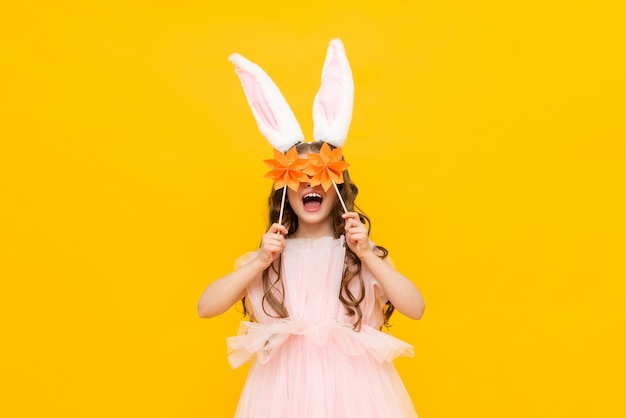 A little girl celebrates Easter A happy smiling child is holding some origami flowers A charming teenager with rabbit ears on a yellow isolated background