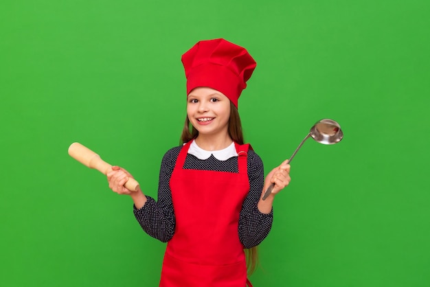 A little girl chef in a red apron and a cooking cap learning to cook on a green isolated background Choosing a profession for a child