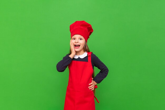 A little girl chef in a red apron and a cooking cap learning to cook on a green isolated background Choosing a profession for a child