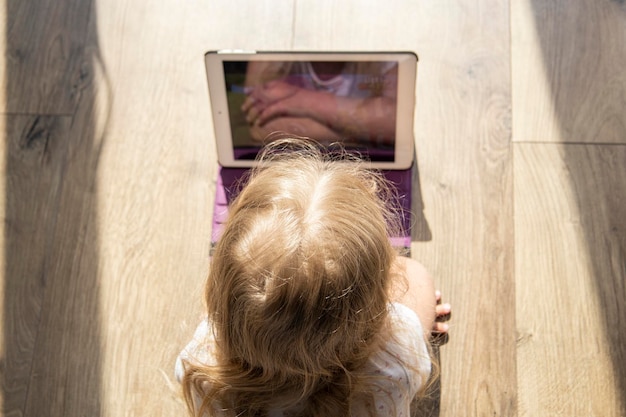 Photo little girl child lying on the floor looks at the tablet top view flat lay