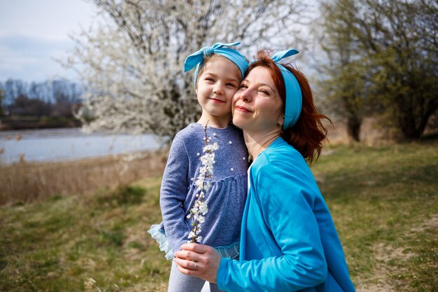 Little girl child and mother woman walks through the spring forest with flowering trees, laugh and play, the beginning of spring, family vacation, love of parents