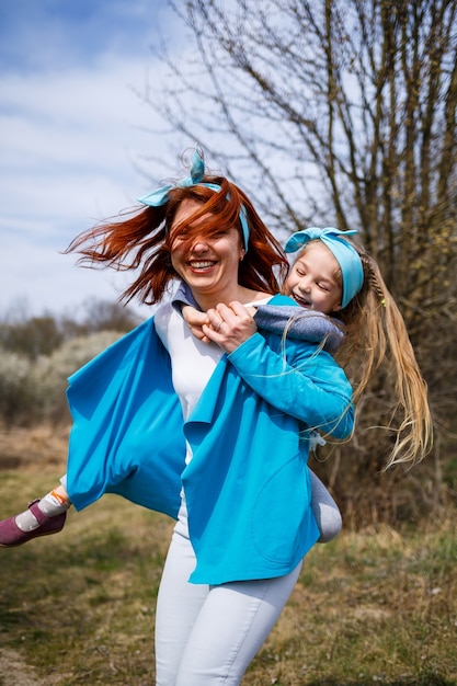 Little girl child and mother woman walks through the spring forest with flowering trees, laugh and play, the beginning of spring, family vacation, love of parents