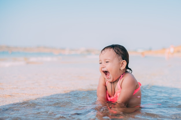 A little girl, a child in a pink swimsuit sitting in the sea is very happy and cheerful