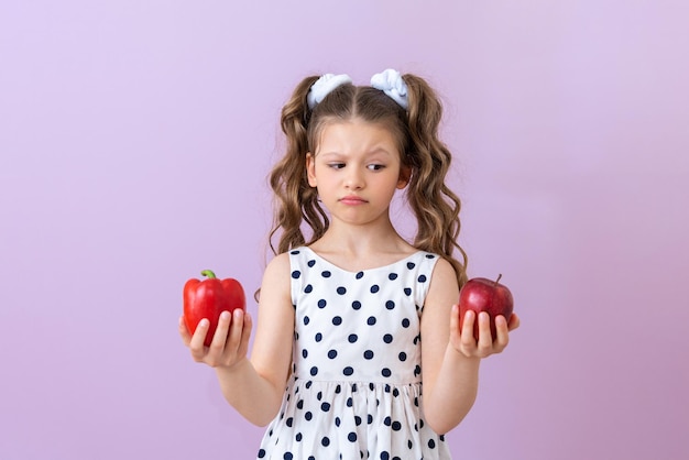 A little girl chooses an apple or a sweet pepper to eat Fruits and vegetables for children's nutrition