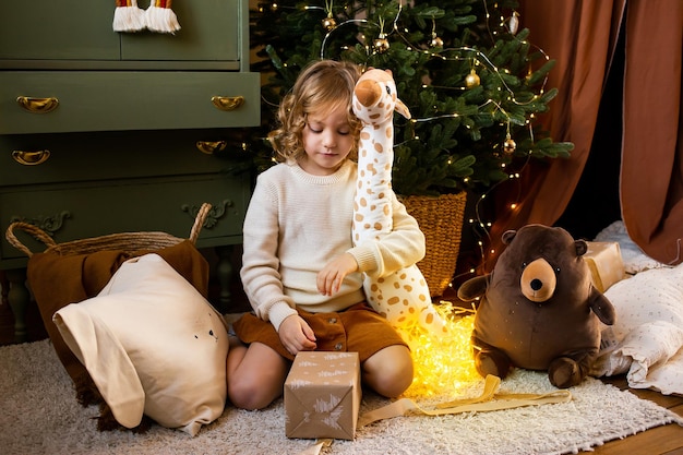 Little girl in Christmas home near festive garland and hugging her cute toys