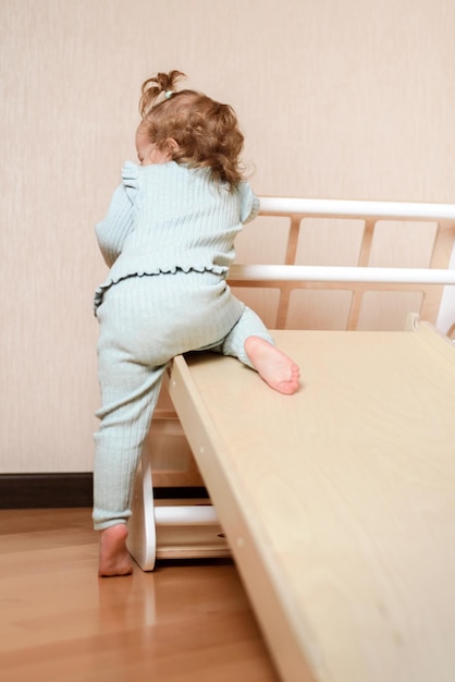 A little girl climbs a wooden slide in the gym The child goes in for sports and develops