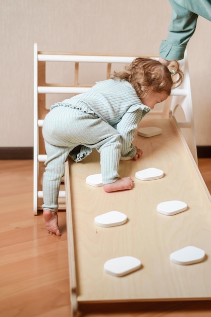 A little girl climbs a wooden slide in the gym The child goes in for sports and develops