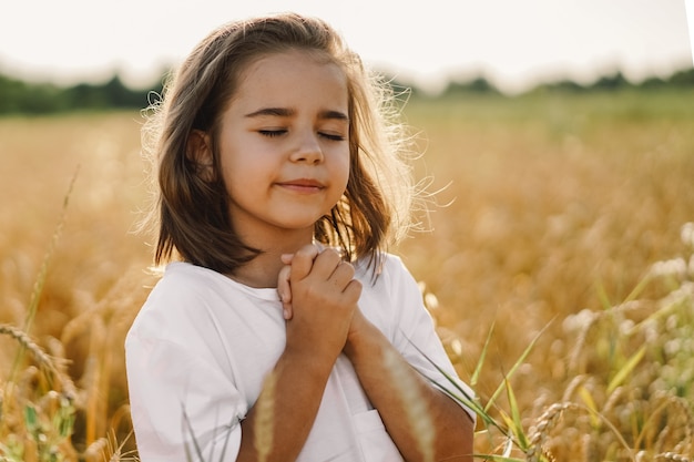 Little Girl closed her eyes, praying in a field wheat. Hands folded in prayer. Religion concept