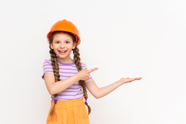 A little girl in a construction helmet holds your advertisement on her hand on a white isolated background The concept of renovation in the children's room