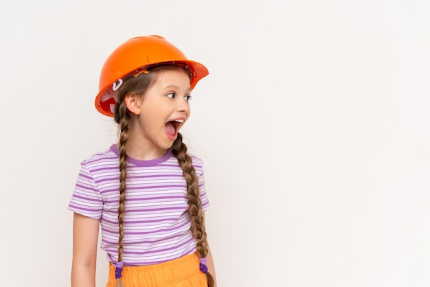 A little girl in a construction helmet looks at your advertisement on a white isolated background Copy space The concept of renovation in the children's room