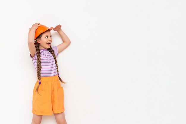 A little girl in a construction helmet looks at your advertisement on a white isolated background Copy space The concept of renovation in the children's room