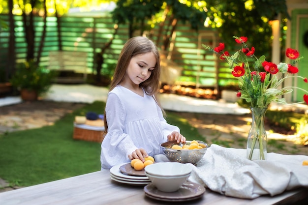 Little girl cooking breakfast in garden summer with fruits on a wooden table in backyard.