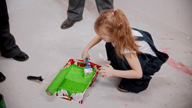 A little girl covering brush in green paint for painting walls