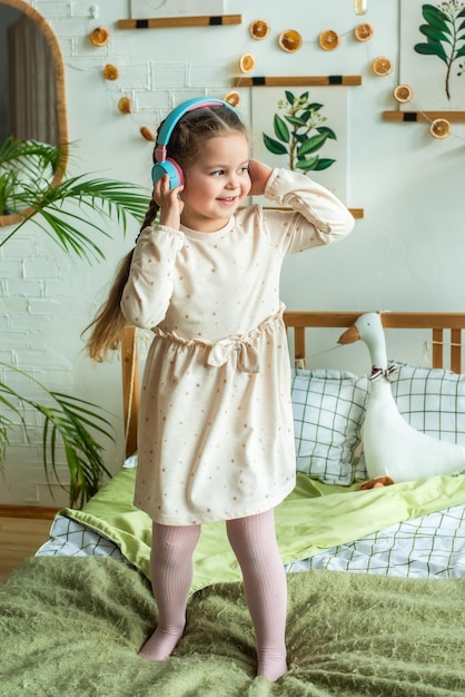 Little girl dances on the bed in headphones baby enjoys listening to music via wireless connection