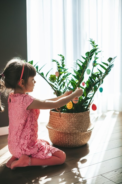 Little girl decorating a plant with Easter eggs