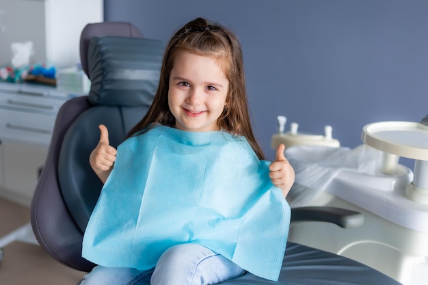 A little girl in a dental chair gives a thumbs up.