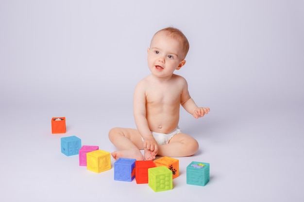 a little girl in a diaper is playing with colorful cubes isolated on a white background