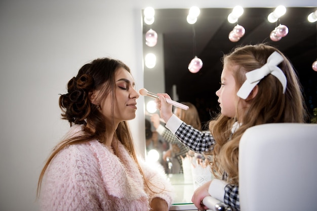 Little girl does makeup for her mom in front of the mirror