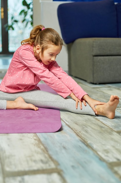 Little girl doing stretching exercises, practicing yoga on fitness mat at home