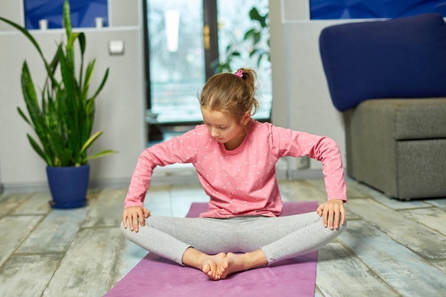 Little girl doing stretching exercises practicing yoga on fitness mat at home