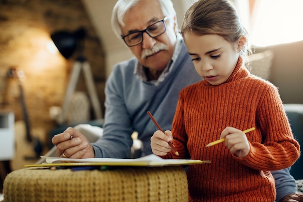 Little girl drawing while spending time with grandfather at home