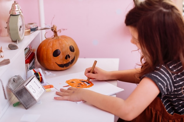 Little girl draws a pumpkin and prepares to celebrate Halloween at home