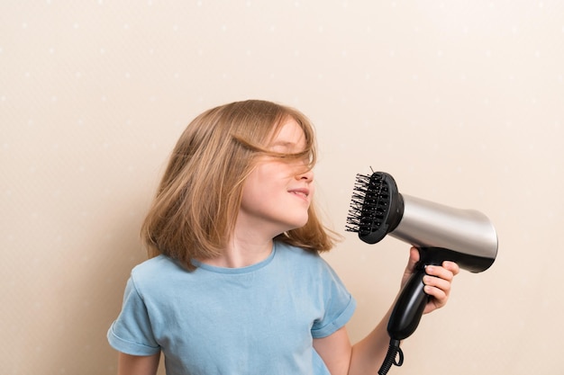 Little girl dries her hair with a hair dryer with a comb attachment