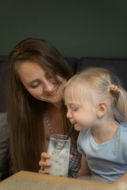 Little girl drinks her mothers cocktail through straw Portrait of young mother and sweet daughter in cafe