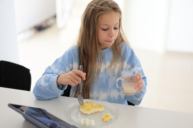 Little girl drinks whole cow39s milk with egg in the morning sitting at the table Proper nutrition for children