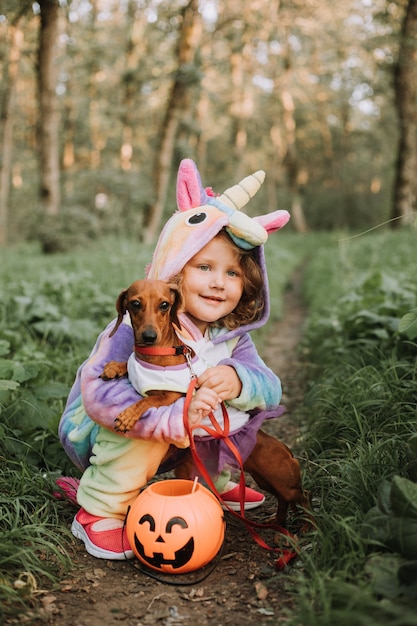 Little girl and a dwarf dachshund in Halloween costumes with a pumpkin basket for sweets outdoors