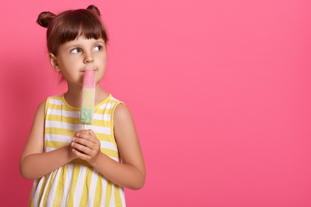 Little girl eating ice cream and looking dreamily aside